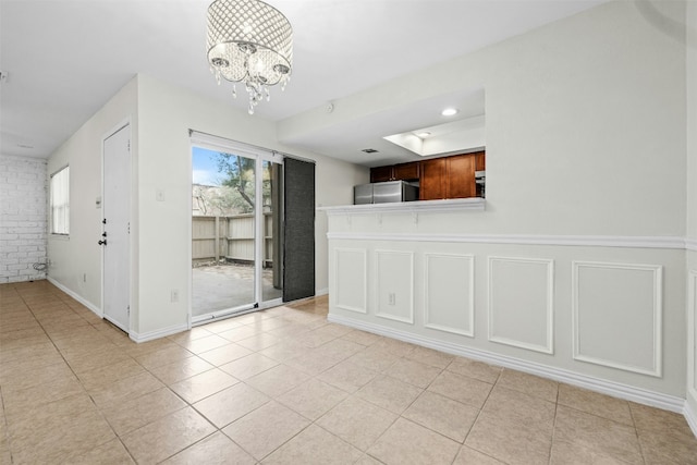 interior space with an inviting chandelier, brick wall, light tile patterned floors, and a decorative wall