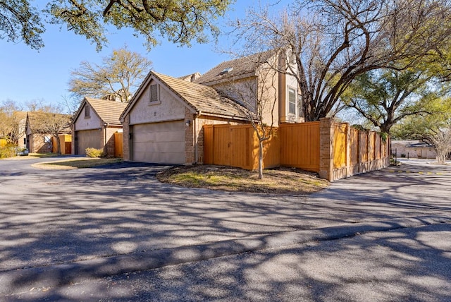 view of home's exterior with aphalt driveway, fence, an attached garage, and stucco siding