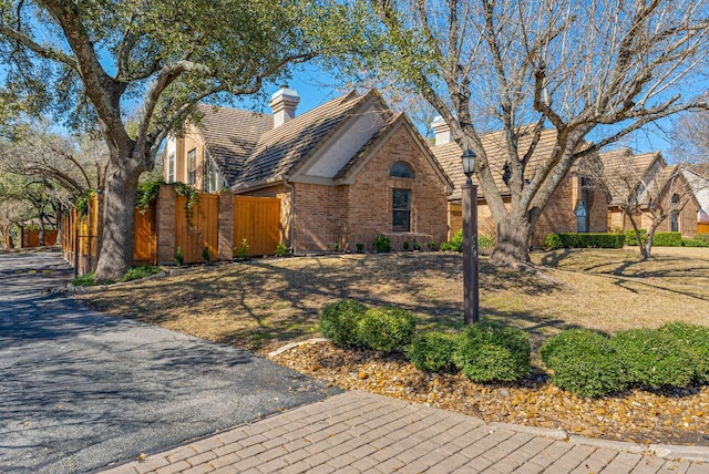 view of front of home featuring brick siding, a chimney, and fence