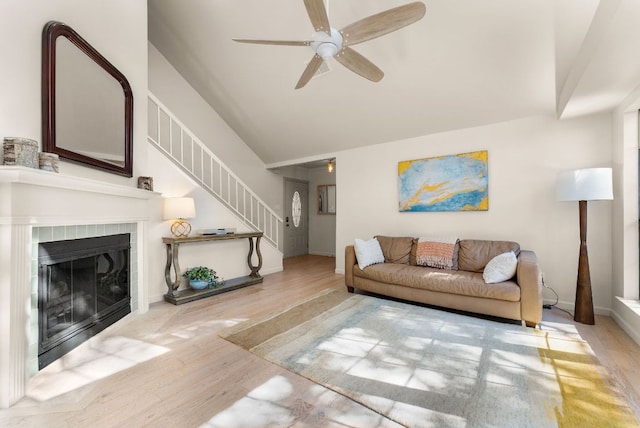 living area with ceiling fan, a fireplace, wood finished floors, stairs, and vaulted ceiling