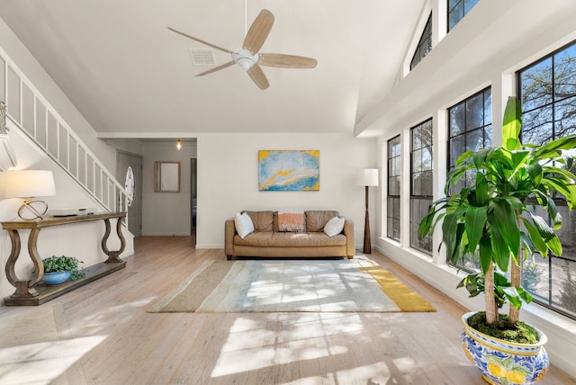 living area featuring visible vents, stairway, a towering ceiling, ceiling fan, and wood finished floors