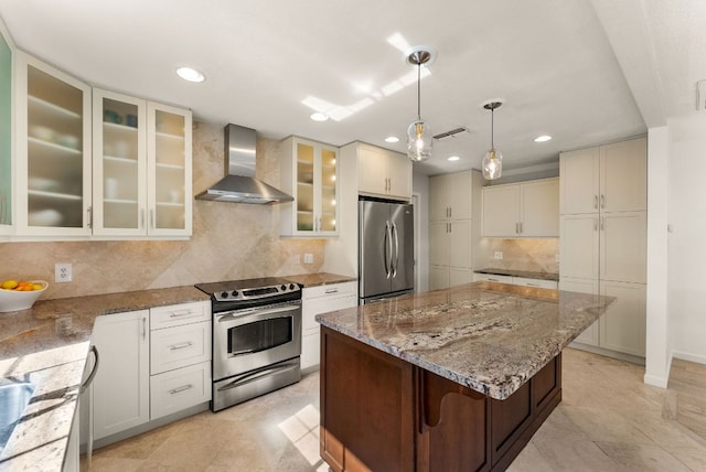 kitchen featuring visible vents, wall chimney exhaust hood, a kitchen island, light stone counters, and stainless steel appliances