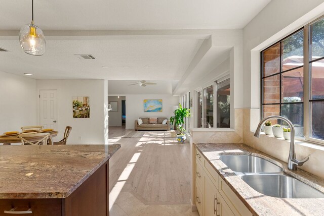 kitchen featuring light stone counters, a healthy amount of sunlight, a sink, and decorative light fixtures