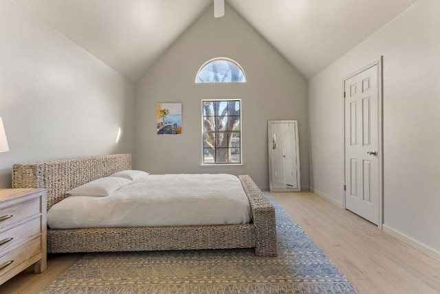 bedroom featuring high vaulted ceiling, light wood-style flooring, and baseboards