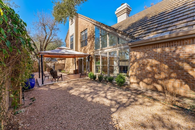 rear view of house with a gazebo, brick siding, a patio, and a chimney