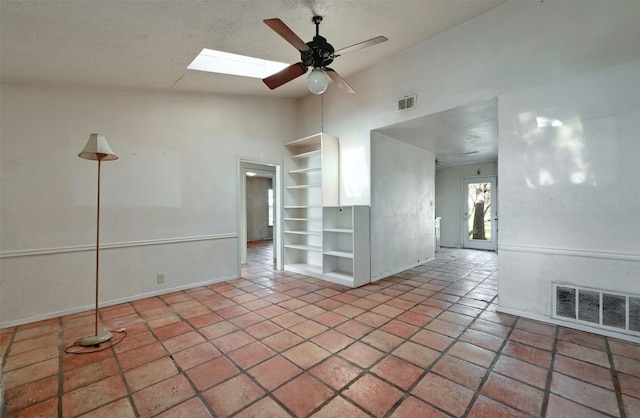 spare room with vaulted ceiling with skylight, visible vents, ceiling fan, and a textured ceiling