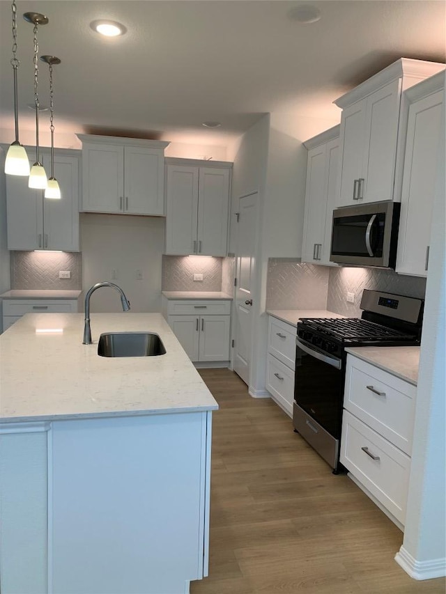 kitchen with decorative backsplash, light wood-style flooring, appliances with stainless steel finishes, a kitchen island with sink, and a sink