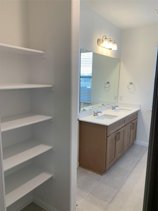 bathroom with double vanity, tile patterned floors, a sink, and baseboards