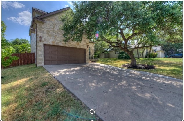 view of front facade featuring a garage, stone siding, a front yard, and fence