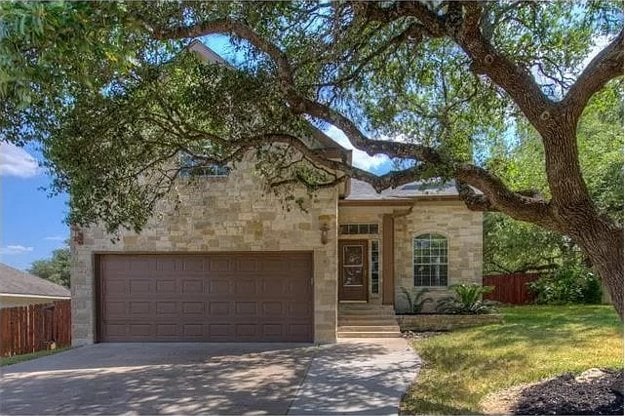 view of front of home featuring concrete driveway, stone siding, an attached garage, fence, and a front yard