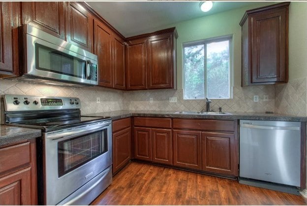 kitchen featuring appliances with stainless steel finishes, a sink, dark wood finished floors, and tasteful backsplash