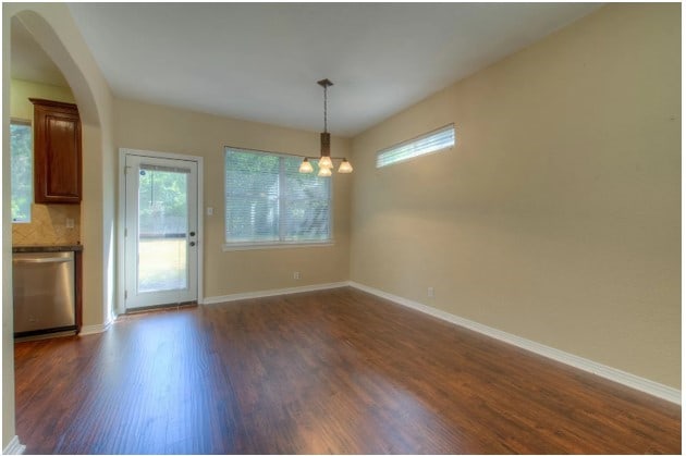 unfurnished dining area with arched walkways, dark wood-type flooring, a chandelier, and baseboards