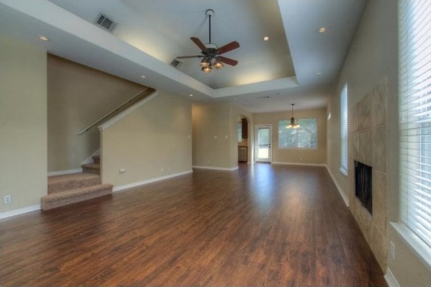 unfurnished living room featuring a tray ceiling, dark wood finished floors, a fireplace, stairway, and baseboards