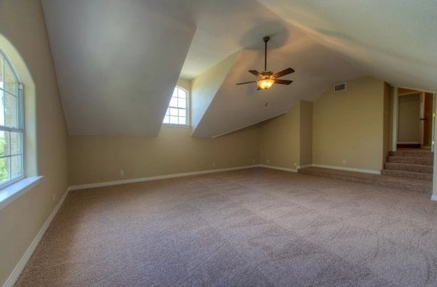 additional living space featuring baseboards, visible vents, vaulted ceiling, and carpet flooring