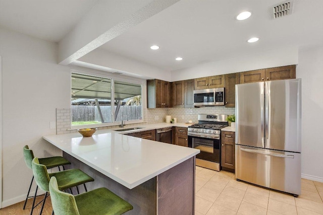 kitchen featuring decorative backsplash, appliances with stainless steel finishes, a breakfast bar, a peninsula, and light countertops