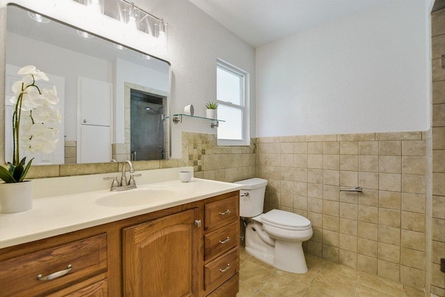 bathroom featuring toilet, a shower with door, tile patterned floors, vanity, and tile walls