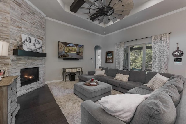 living area with ceiling fan, arched walkways, a stone fireplace, wood finished floors, and a tray ceiling