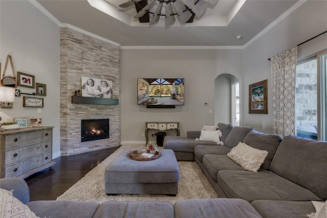 living area featuring ceiling fan, a raised ceiling, a fireplace, arched walkways, and wood finished floors