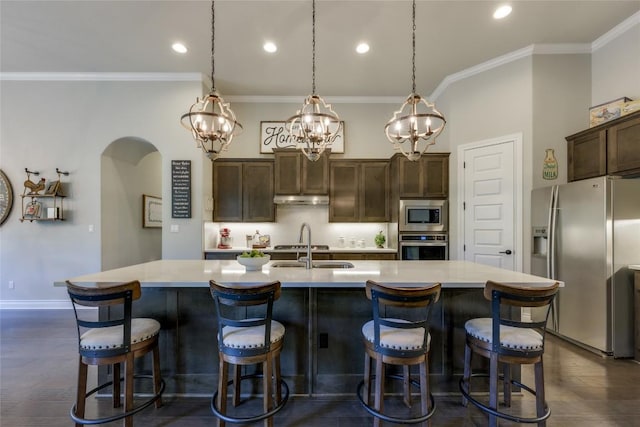 kitchen featuring crown molding, appliances with stainless steel finishes, arched walkways, dark brown cabinets, and light countertops