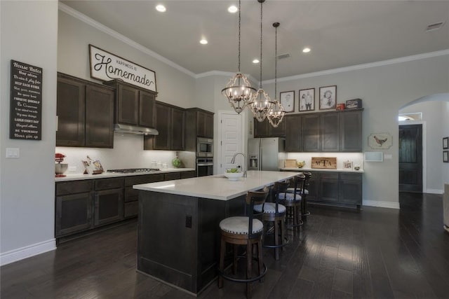 kitchen with arched walkways, ornamental molding, stainless steel appliances, and under cabinet range hood