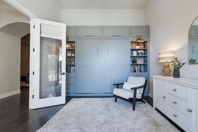sitting room featuring arched walkways, baseboards, and dark wood-style floors
