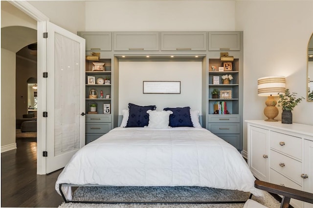 bedroom with arched walkways and dark wood-type flooring