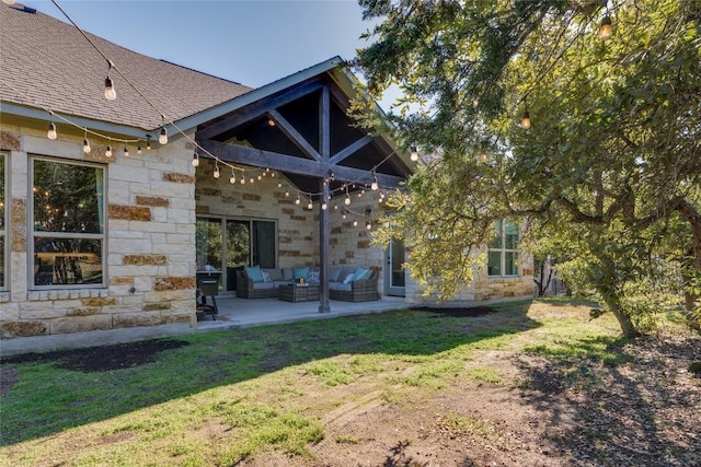 back of property featuring roof with shingles, stone siding, an outdoor living space, a lawn, and a patio