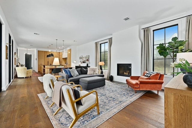 living area featuring visible vents, dark wood-style flooring, and a glass covered fireplace