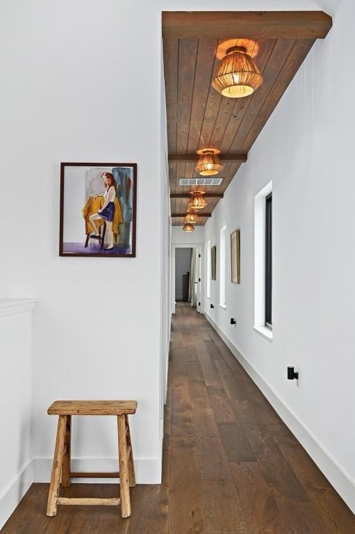 hallway featuring beamed ceiling, wood finished floors, wood ceiling, and baseboards