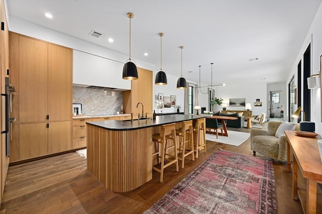 kitchen featuring dark wood-style floors, a breakfast bar area, dark countertops, decorative backsplash, and a sink