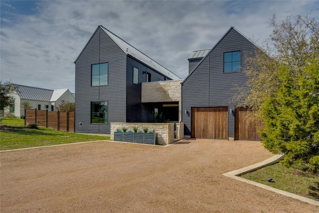 rear view of property featuring metal roof, a garage, fence, driveway, and a standing seam roof