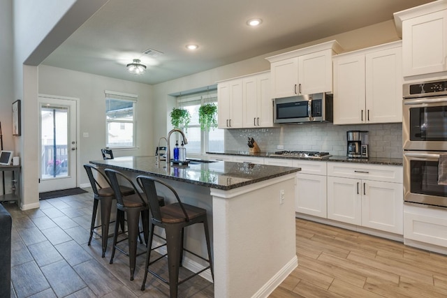 116 Evening Star Ln, Georgetown, TX 78628 - kitchen featuring appliances with stainless steel finishes, a sink, a center island with sink, backsplash, and light wood-type flooring