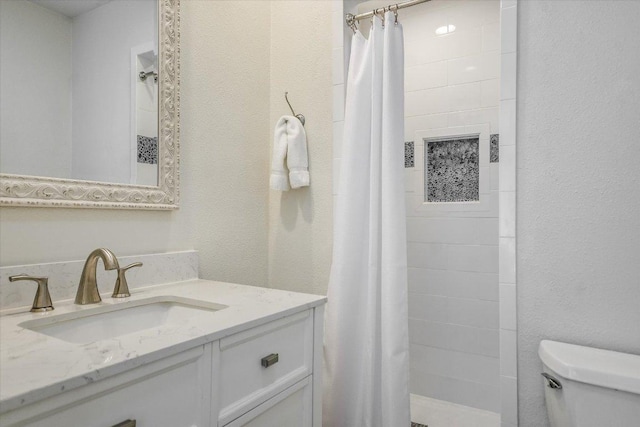 bathroom with toilet, a tile shower, and vanity