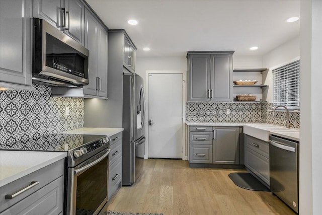 kitchen featuring light wood finished floors, stainless steel appliances, a sink, and gray cabinetry