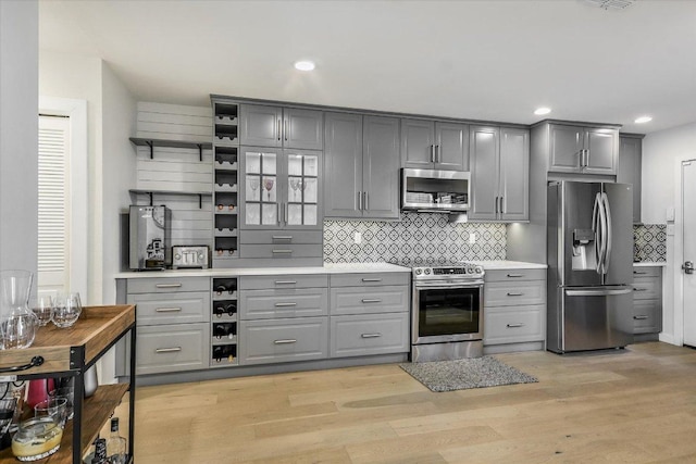 kitchen featuring stainless steel appliances, open shelves, light wood-type flooring, and gray cabinets