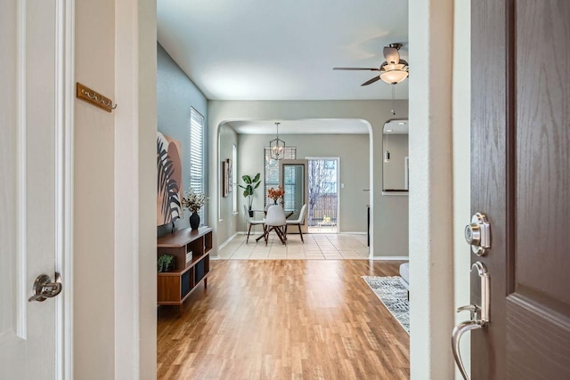 foyer entrance with light wood finished floors, ceiling fan, baseboards, and arched walkways