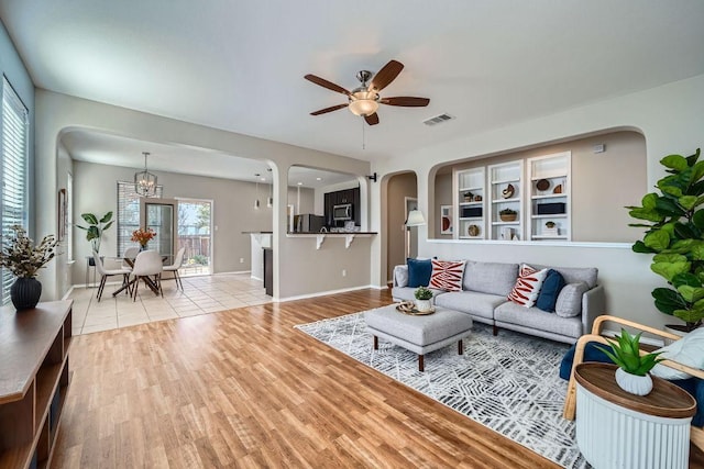 living area with arched walkways, visible vents, wood finished floors, baseboards, and ceiling fan with notable chandelier