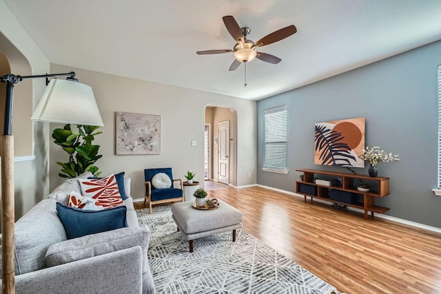 living room featuring arched walkways, wood finished floors, a ceiling fan, and baseboards