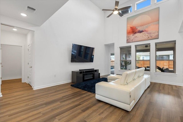 living area featuring ceiling fan, a high ceiling, baseboards, wood finished floors, and visible vents