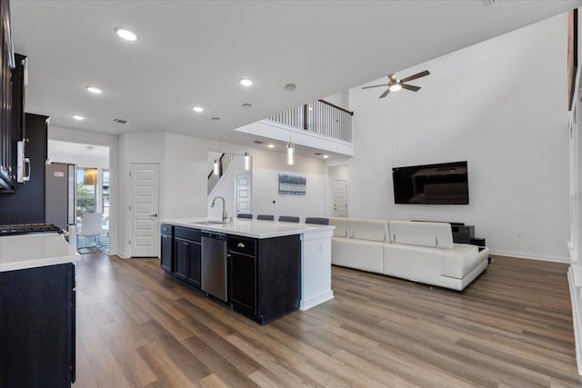 kitchen with a kitchen island with sink, a ceiling fan, wood finished floors, dishwasher, and a sink