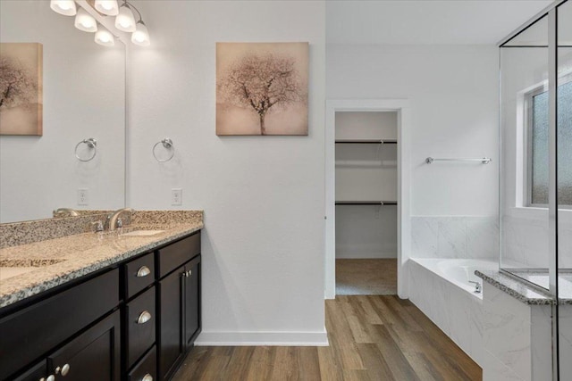 full bath featuring a walk in closet, a sink, double vanity, wood finished floors, and a garden tub