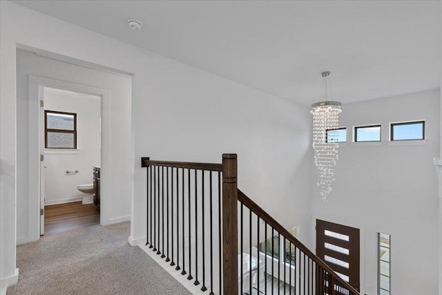 hall featuring a notable chandelier, an upstairs landing, baseboards, and carpet