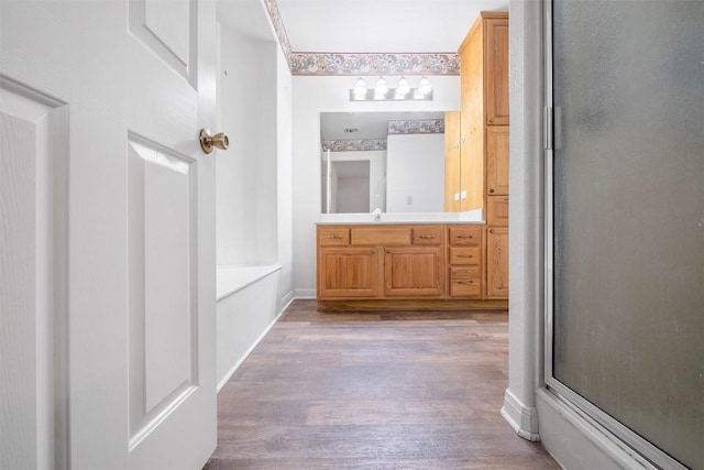 bathroom with a shower with door, a bathing tub, vanity, wood finished floors, and baseboards
