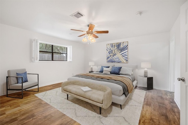 bedroom featuring a ceiling fan, visible vents, baseboards, and wood finished floors