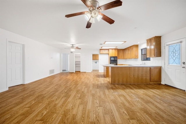 kitchen with black microwave, a peninsula, visible vents, light wood-style floors, and light countertops