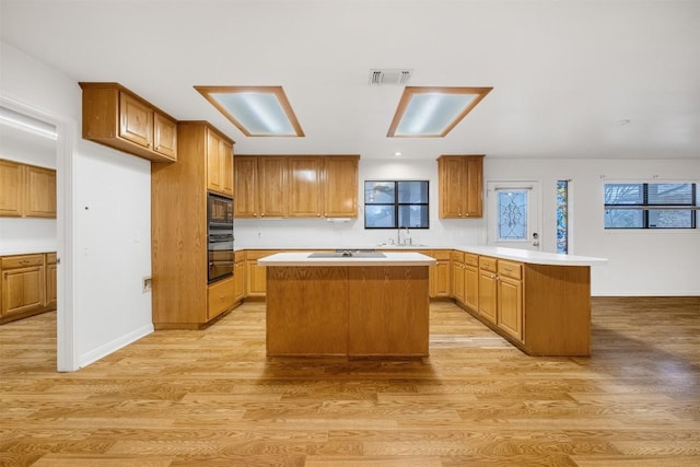 kitchen with a peninsula, visible vents, light countertops, light wood-type flooring, and a center island