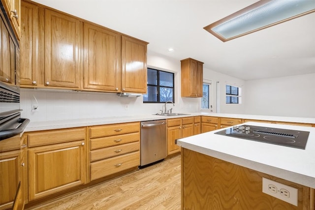 kitchen featuring light wood finished floors, light countertops, a sink, dishwasher, and black electric cooktop