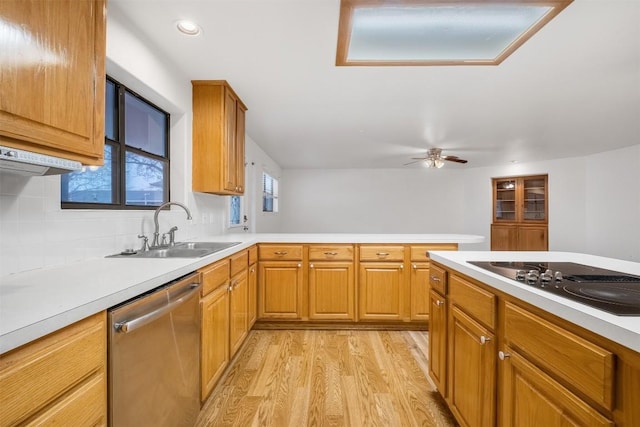 kitchen featuring light countertops, stainless steel dishwasher, light wood-style floors, a sink, and black electric cooktop
