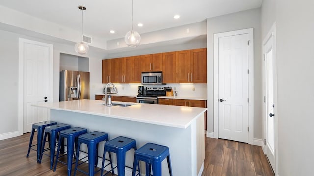 kitchen with a sink, visible vents, appliances with stainless steel finishes, brown cabinets, and dark wood-style floors