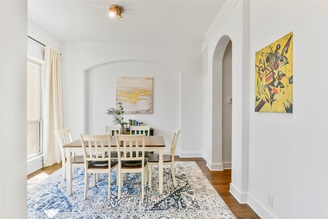 dining space featuring arched walkways, dark wood-type flooring, crown molding, and baseboards